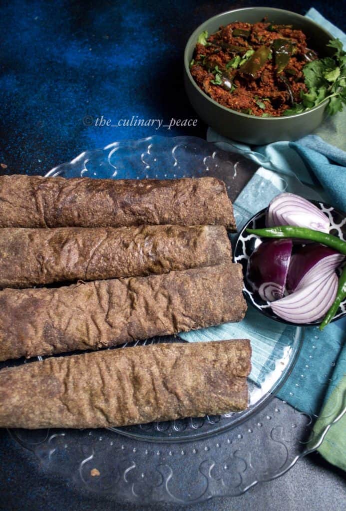 Power packed, healthy recipe of soft Ragi Roti rolled and placed on a glass plate along with onion, green chilies against a blue background